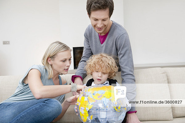 Eltern im Wohnzimmer mit ihrem Sohn  der einen Globus hält