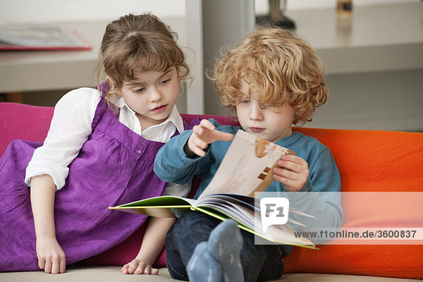 Junge sitzt mit seiner Schwester und liest ein Buch.