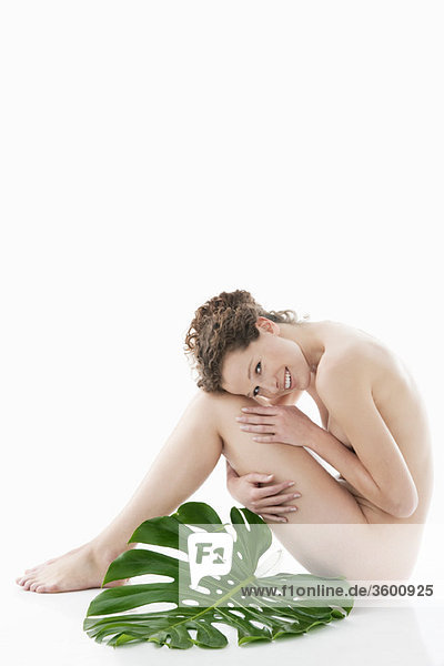 Nackte Frau sitzend mit einem Philodendronblatt neben ihr