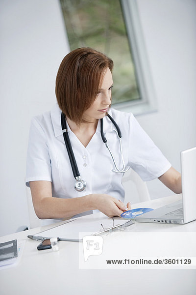 Female doctor sitting in an office inserting CD into a laptop