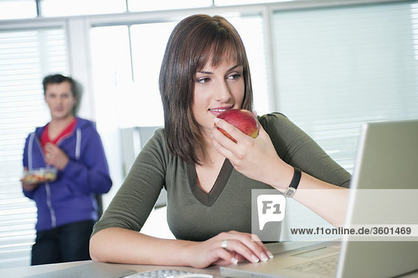 Geschäftsfrau  die einen Apfel isst und einen Laptop benutzt