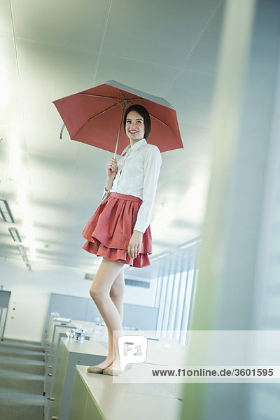 Geschäftsfrau  die einen Schirm hält und auf einem Schreibtisch im Büro steht.