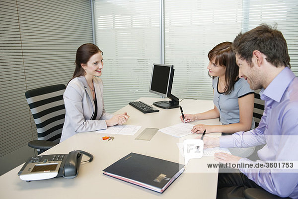 Couple signing agreement form in a real estate agent's office