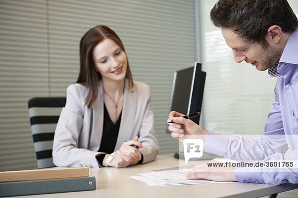 Man signing documents with a female real estate agent sitting in front of him
