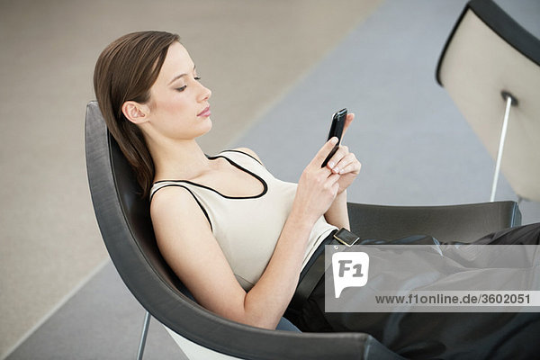 Frau liegt in einem Stuhl und SMS mit einem Handy