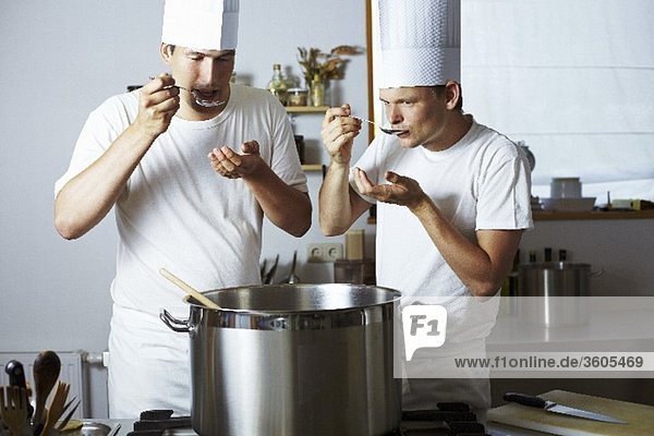 Two chefs tasting soup out of pan