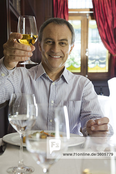 Ein reifer Mann  der ein Glas Wein zum Feiern aufzieht.