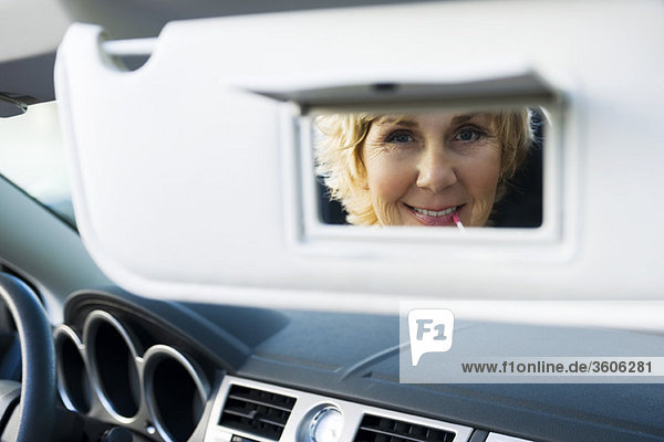 Frau im Auto mit Visier-Eitelkeitsspiegel zum Auftragen von Make-up und Mund