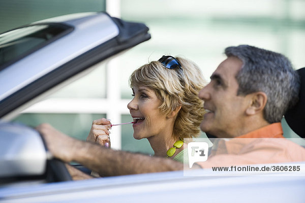 Mature couple in car together  woman putting on lip gloss