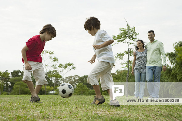 Jungen spielen Fußball  Eltern sehen im Hintergrund zu.