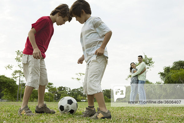 Jungen spielen Fußball  Eltern umarmen sich im Hintergrund