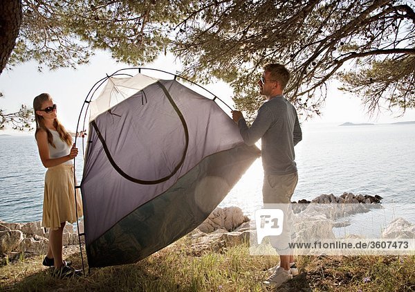 Couple putting up tent by sea