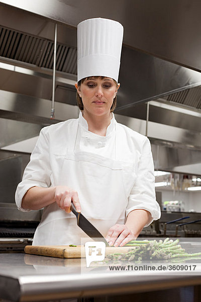 Female chef chopping asparagus in commercial kitchen