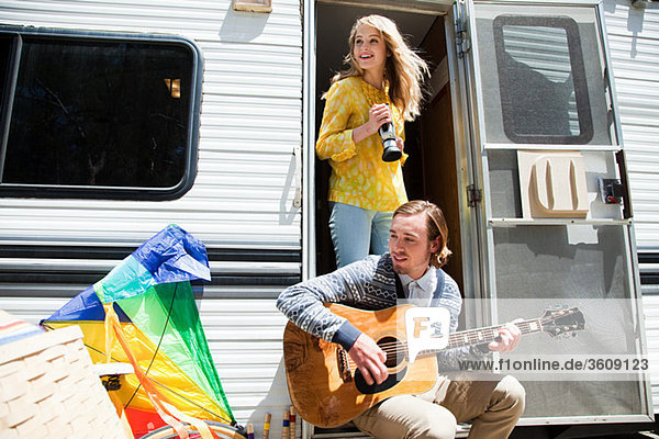 Young couple by caravan with guitar and video camera