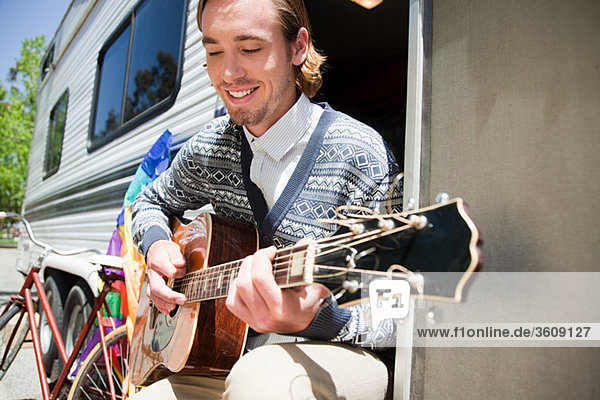 Young man playing guitar by caravan