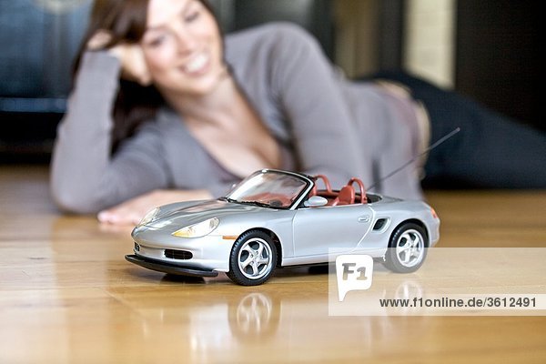 Frau liegt auf dem Fußboden und schaut auf Modellauto