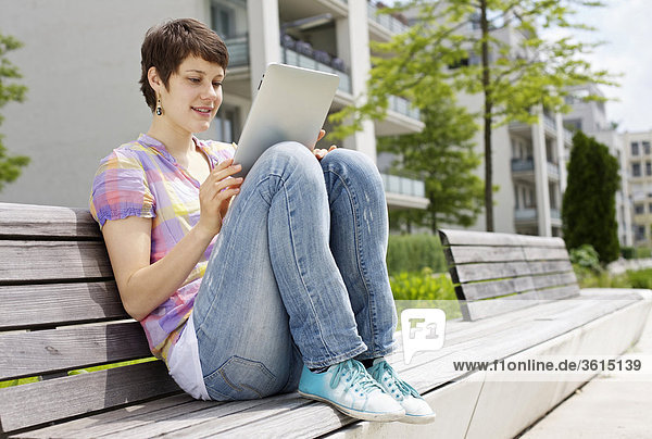 Junge Frau benutzt einen iPad auf einer Bank