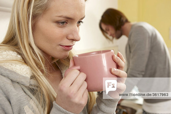 Junge Frau trinkt Kaffee in der Küche mit Mann im Hintergrund