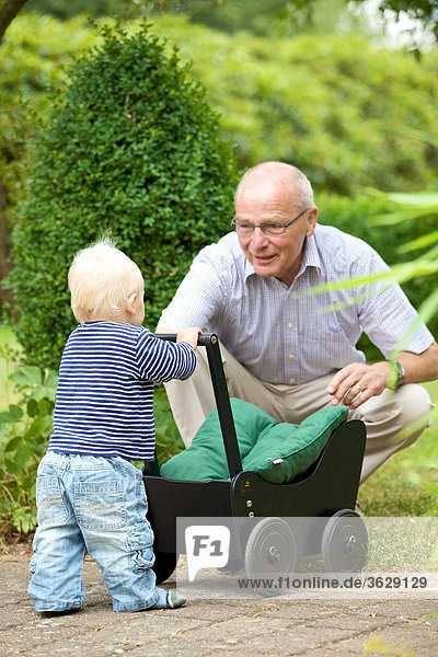 Grandfather and toddler with doll's pram outdoors