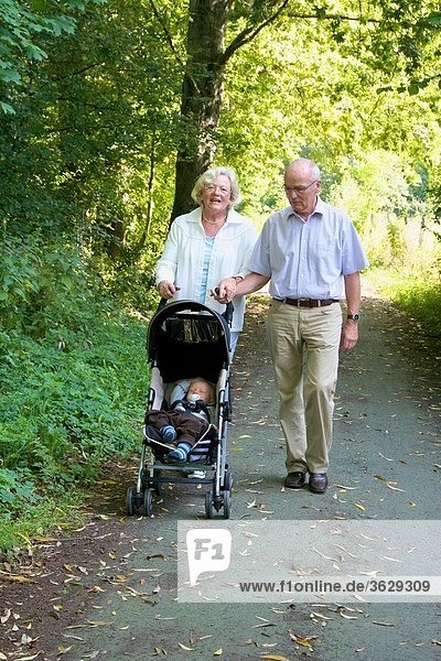 Großeltern gehen mit Enkelsohn im Kinderwagen spazieren