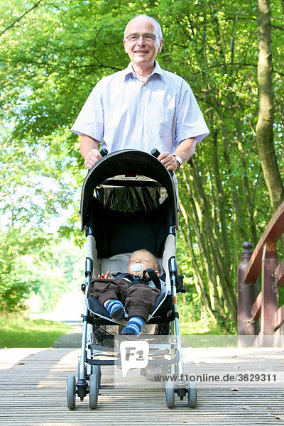Grandfather going for a walk with grandson in pushchair