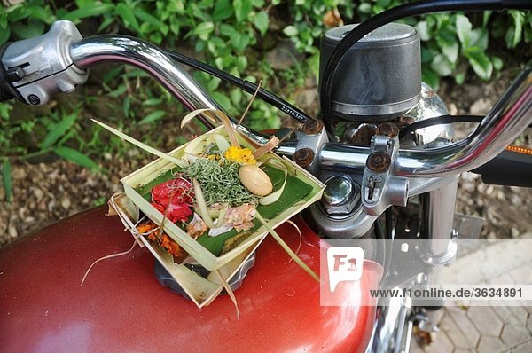 Ubud (Bali  Indonesia): two canangs  little trays made with banana tree leaves and filled with offerings to the spirits  left by a Hindu believer on a motor-bike´s tank