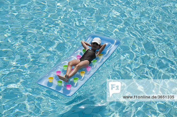 Mädchen  acht Jahre  relaxt auf Luftmatratze im Pool