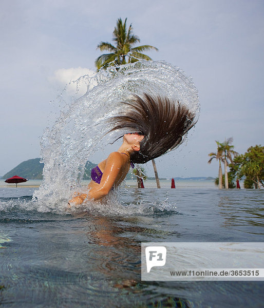 A girl  about 16 years  throwing her hair in the air in a pool of water