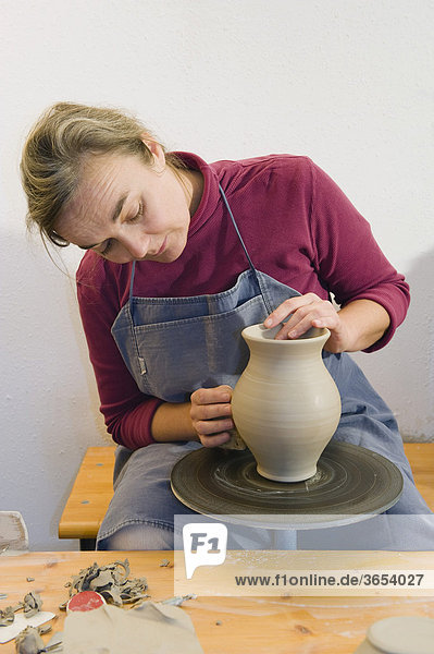 Keramikerin arbeitet in ihrer Werkstatt auf der Drehscheibe  poliert Oberfläche eines Krugs  Geisenhausen  Bayern  Deutschland  Europa