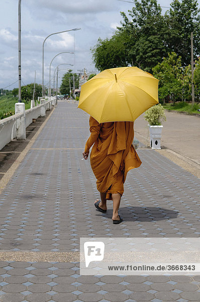 Mönch mit Schirm und Zigarette geht auf Promenade  Nong Khai  Thailand  Asien