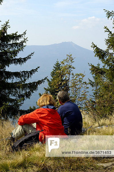 Couple rests from hiking in the grass with a view to Grosser Arber from Grosser Falkenstein Bayerischer Wald Lower Bavaria Germany