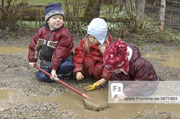 Kinder spielen bei schlechtem Wetter im Regen in Pfützen und im Matsch Schlamm