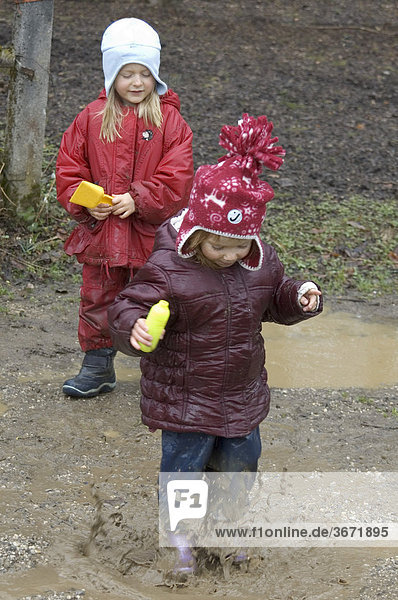 Kinder spielen bei schlechtem Wetter im Regen in Pfützen und im Matsch Schlamm