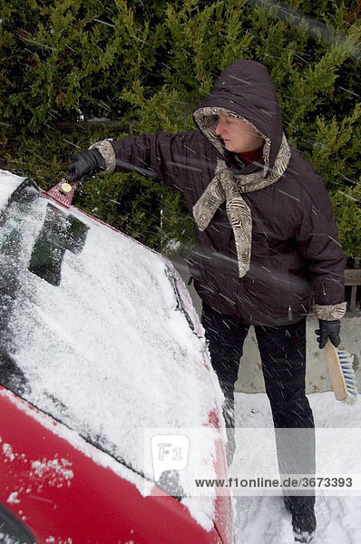Woman removes snow and ice from a car