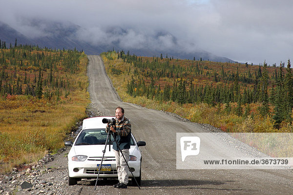 Fotograf steht vor seinem Mietauto auf der Schotterpiste des Denali Highways Alaska USA