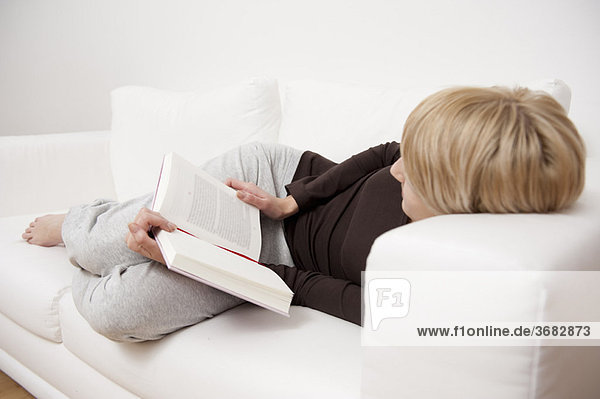 Frau beim Lesen eines Buches auf dem Sofa