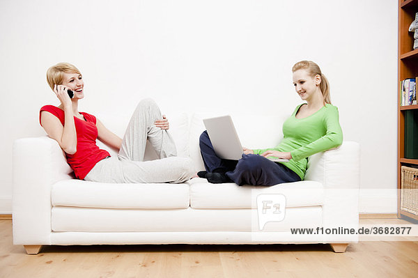 Zwei Frauen mit Laptop und Telefon auf dem Sofa