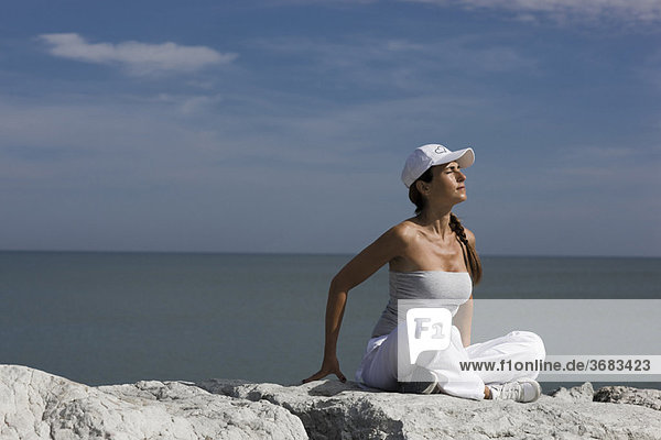 Frau auf Felsen am Meer sitzend