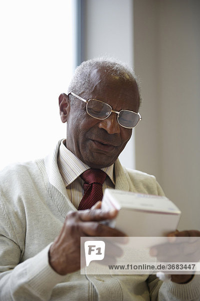 Elderly black man reading medicine box
