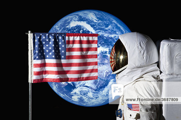 Ein Astronaut steht bei einer amerikanischen Flagge mit der Erde im Hintergrund.
