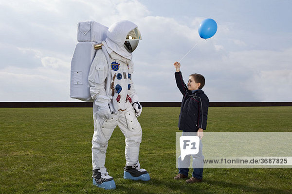 Ein Junge hält einem Astronauten einen Ballon entgegen.