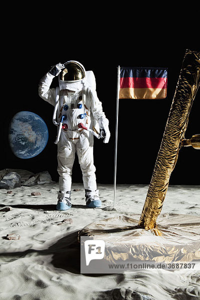 Ein Astronaut  der in der Nähe einer Mondlandefähre steht  grüßt eine deutsche Flagge.