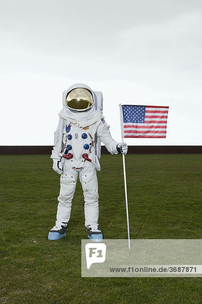 Ein Astronaut steht auf einem Rasen und posiert neben einer amerikanischen Flagge.
