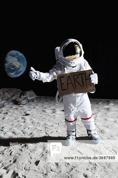 Ein Astronaut auf dem Mond mit ausgestrecktem Daumen  der das Zeichen'EARTH' hält.