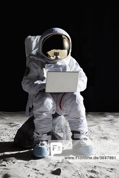 Ein Astronaut auf dem Mond  der mit einem Laptop auf einem Felsen sitzt.
