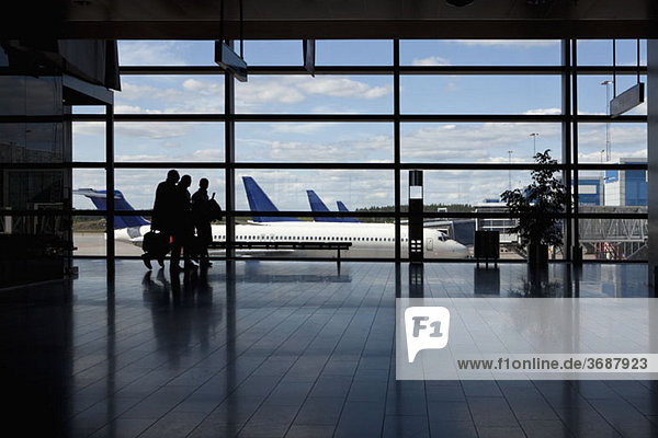Drei Geschäftsleute  die am Fenster eines Flughafens vorbeigehen  Silhouette