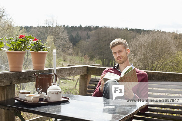 Ein Mann sitzt an einem Tisch auf einem Balkon und liest.