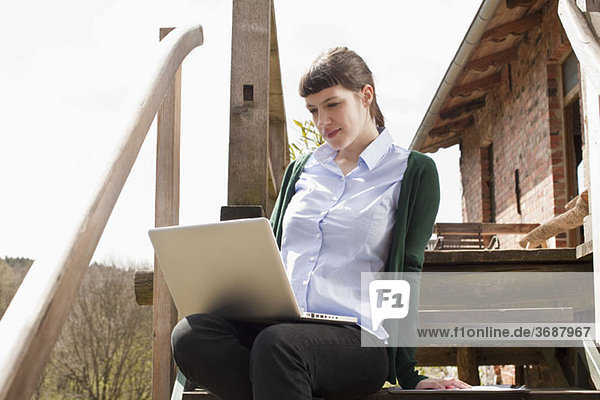 A woman sitting on a staircase  looking at a laptop