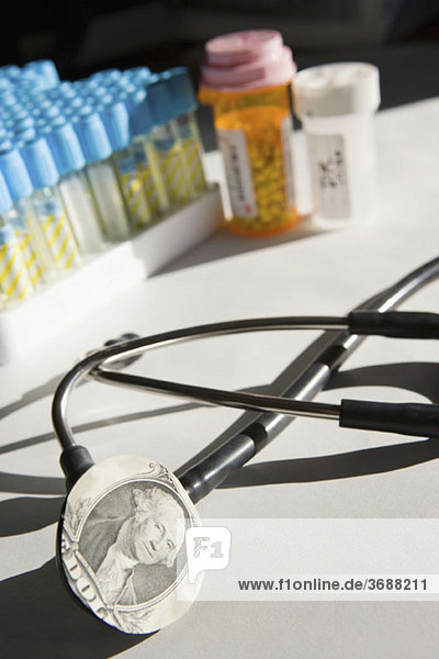 Ein Stethoskop mit Dollarschein und Medizin im Hintergrund.