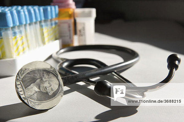 Ein Stethoskop mit Dollarschein und Medizin im Hintergrund.